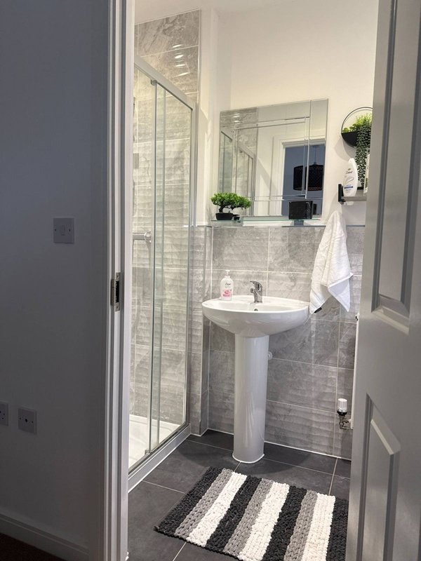 Modern bathroom with pedestal sink, glass shower enclosure, mirror and striped floor mat