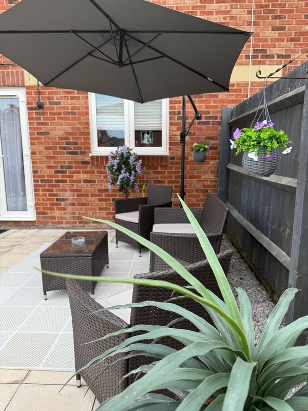 Brick patio with black umbrella, rattan furniture, potted plants and hanging baskets