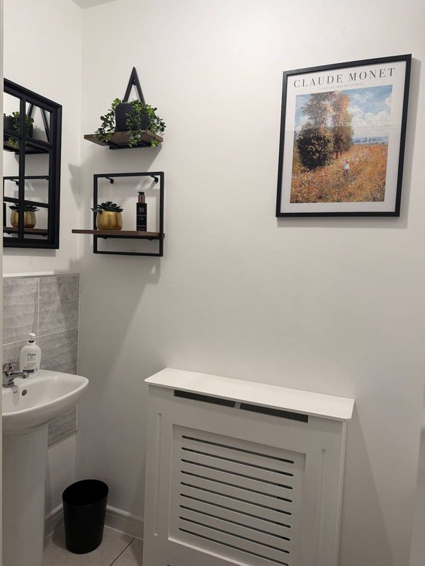 Modern bathroom with wall-mounted shelves, framed artwork, sink and radiator cover