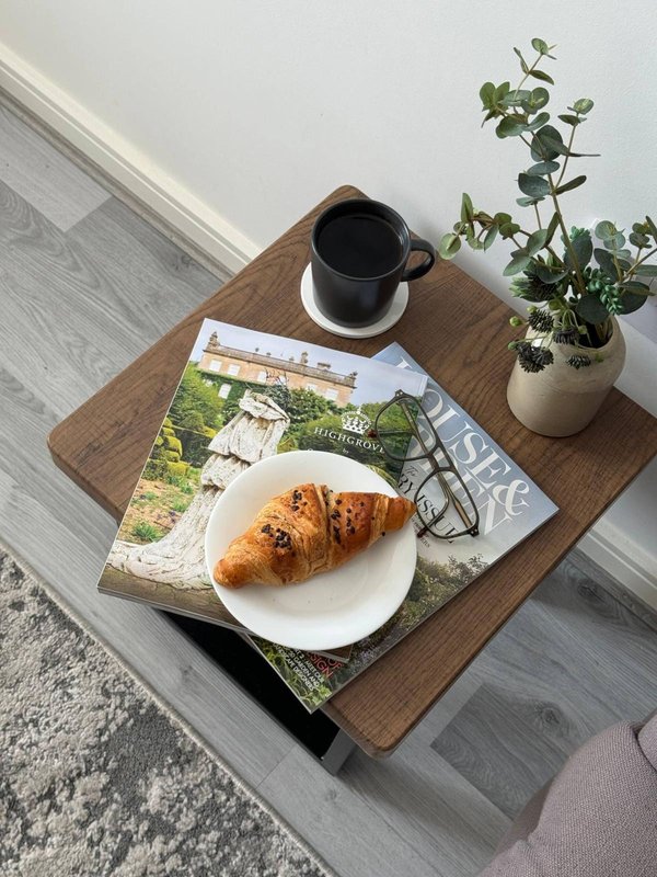 Wooden table with coffee mug, croissant on plate, magazine and potted plant