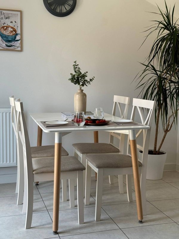 Modern dining area with white table, wooden legs, white chairs, potted plants and wall clock