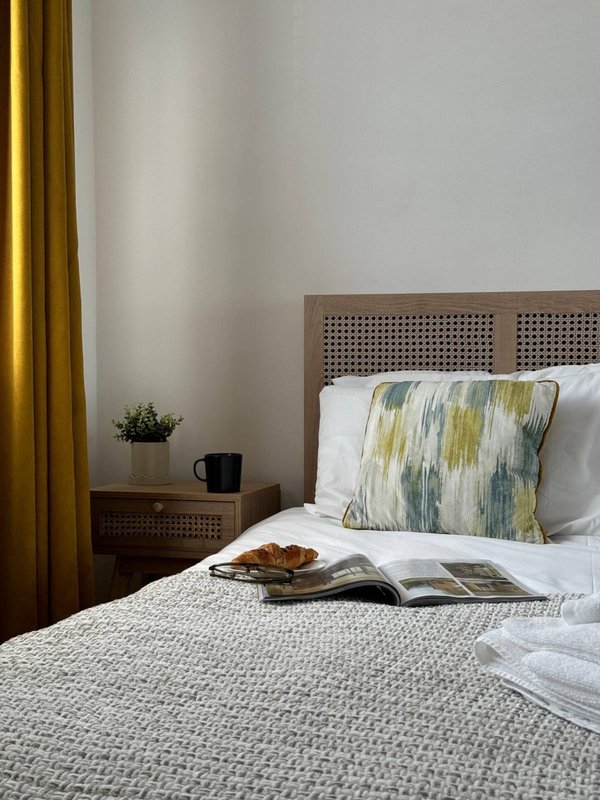 Bedroom with wooden headboard, patterned pillow, open magazine on bed, and gold curtains
