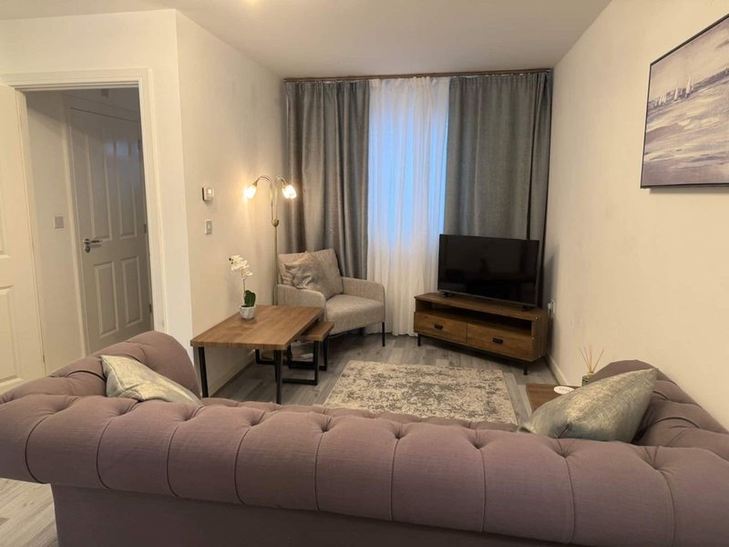Living room with purple sofa, wooden TV stand, armchair, and window with grey curtains