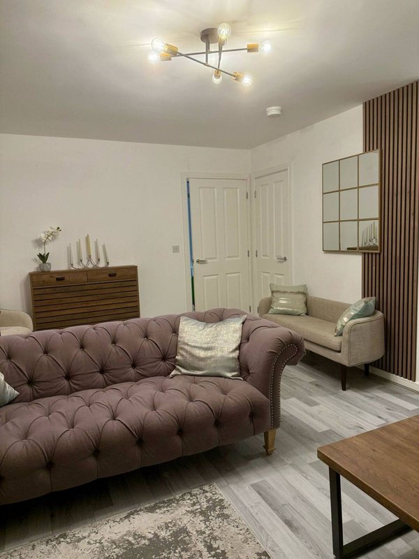 Modern living room with purple tufted sofa, beige armchair, wooden dresser, and brass ceiling light