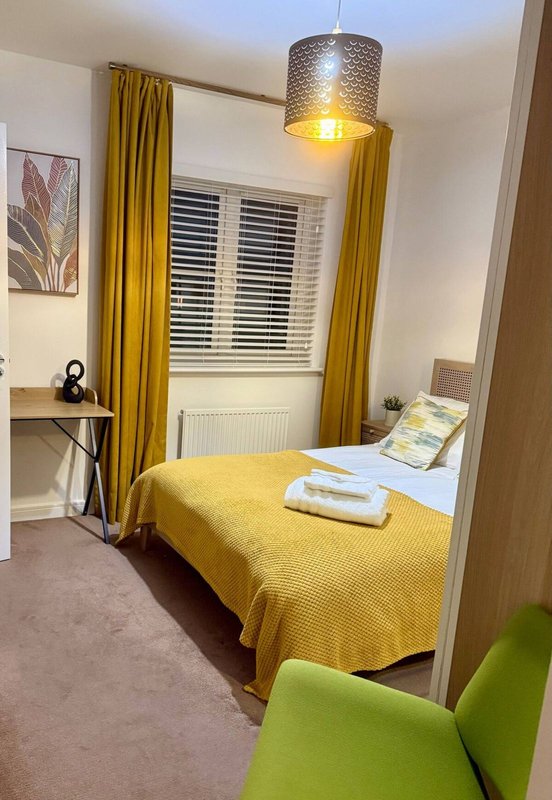 Bedroom with single bed, yellow bedspread, desk, pendant light and shuttered window