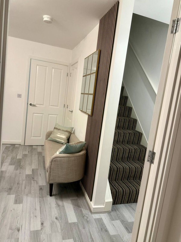 Modern hallway with striped staircase, upholstered chair, white doors and gray flooring