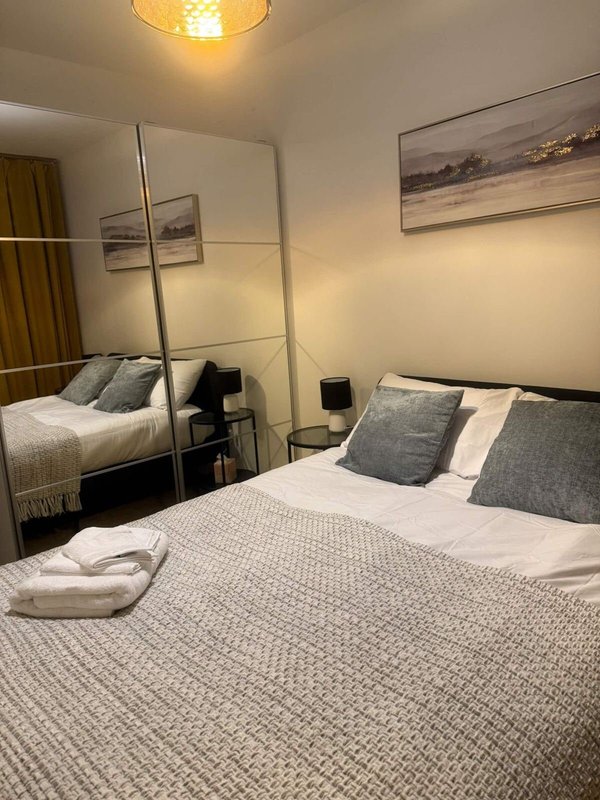 Modern bedroom with double bed, grey bedding, mirrored wardrobe and framed landscape artwork
