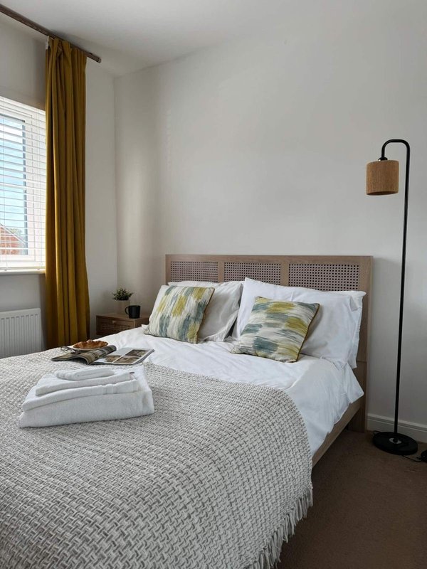 Bright bedroom with double bed, rattan headboard, patterned pillows and floor lamp