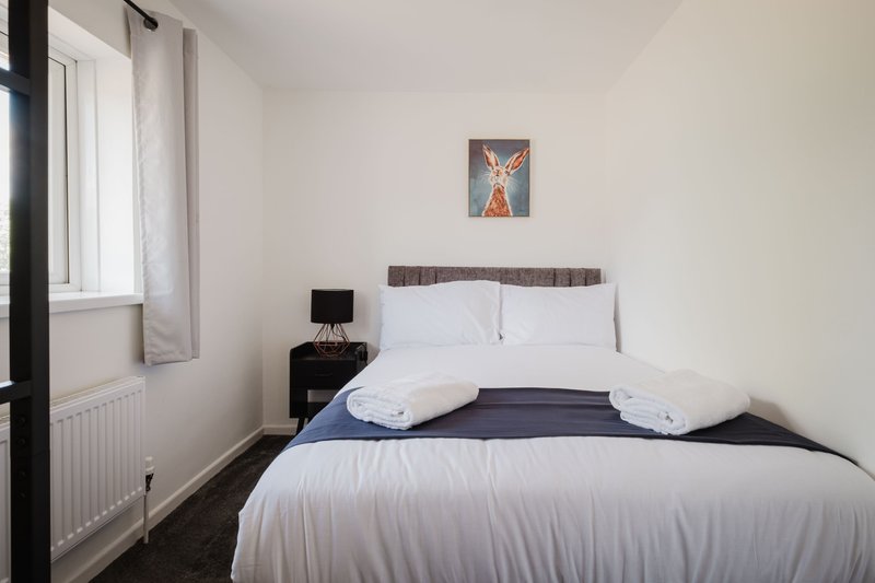 Bedroom with double bed, white bedding, dark headboard, small bedside table and window