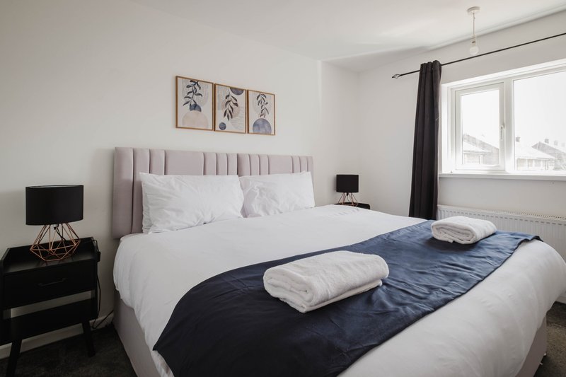 Modern bedroom with gray upholstered headboard, white bedding, dark blue throw, and black nightstand