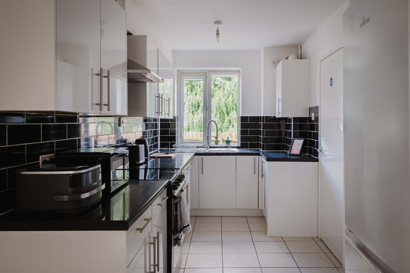 Modern white kitchen with black tile backsplash, stainless steel appliances and garden view