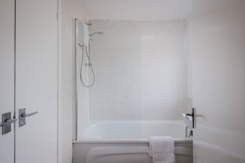 Modern bathroom with white tile walls, bathtub with glass shower enclosure and handheld showerhead