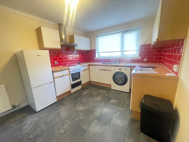 Kitchen with white appliances, red brick splashback, washing machine, and dark flooring