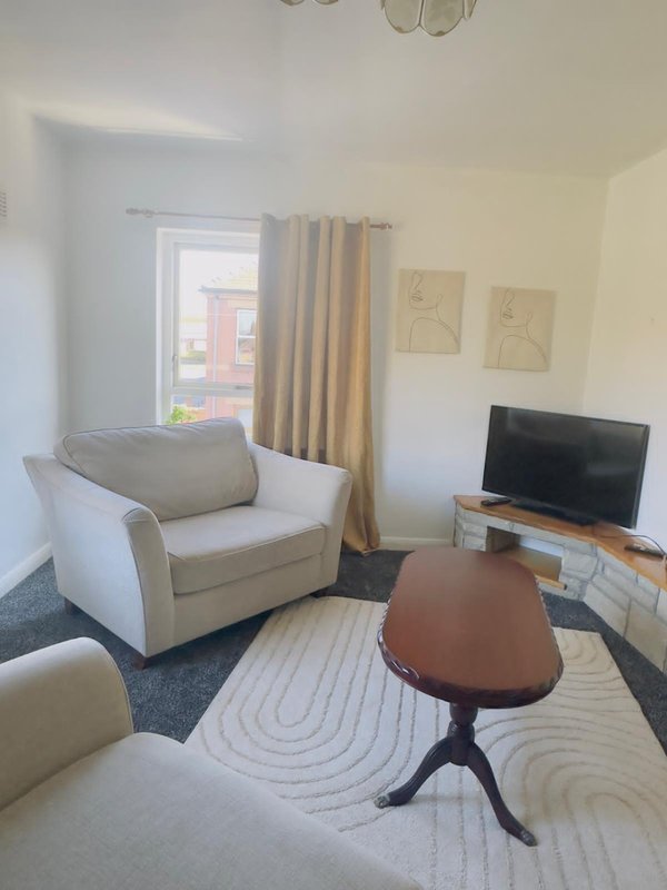 Living room with cream armchair, wooden coffee table, TV on stand, and window with curtains