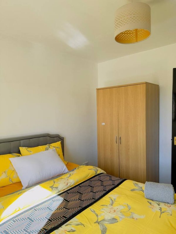 Bright bedroom with yellow star bedding, wooden wardrobe, and woven ceiling lamp
