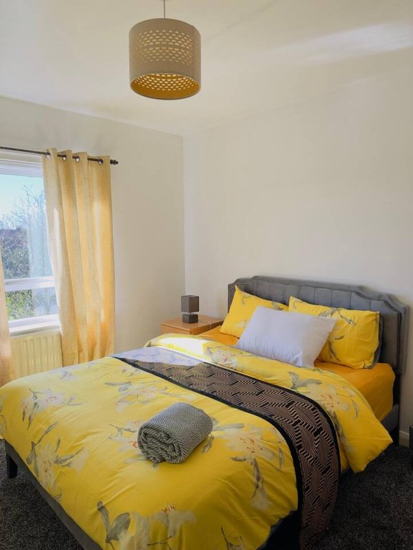 Bright bedroom with yellow bedding, gray headboard, pendant lamp, and window with curtains