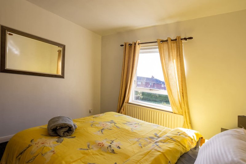 Bright yellow bedroom with double bed, window with gold curtains and radiator