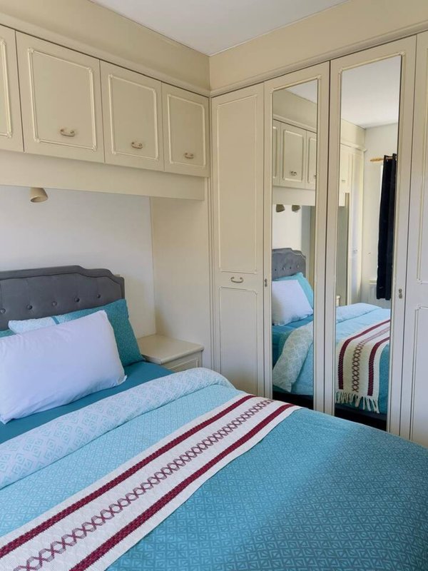 Compact bedroom with single bed, turquoise bedding, built-in wardrobes and mirrored door