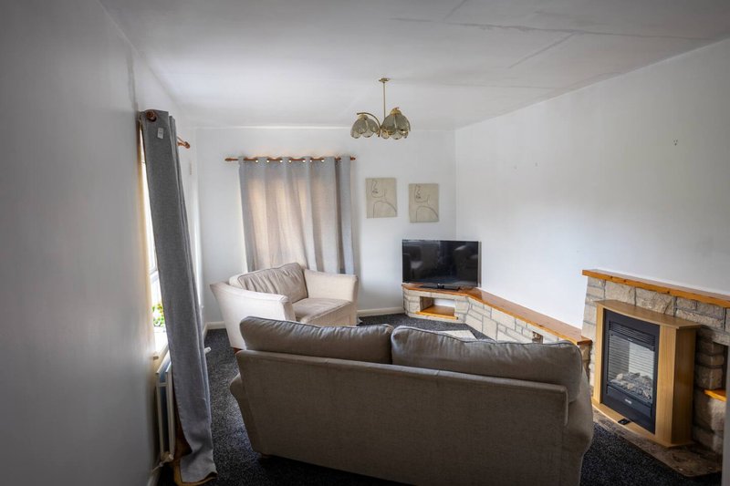 Living room with brown leather sofa, fireplace, TV, pendant light and window