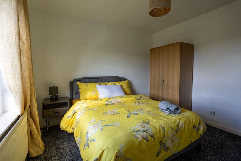 Bright bedroom with double bed, yellow floral duvet, wooden wardrobe and window