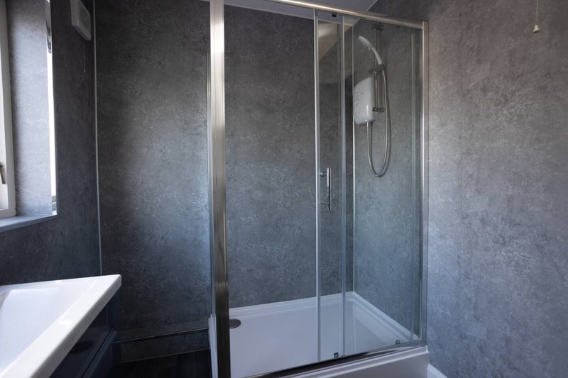 Modern bathroom with glass shower enclosure, dark tile walls and white basin