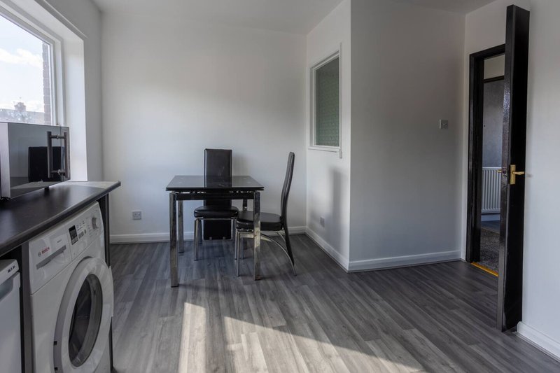 Open-plan kitchen and office space with washing machine, desk, chair and grey flooring