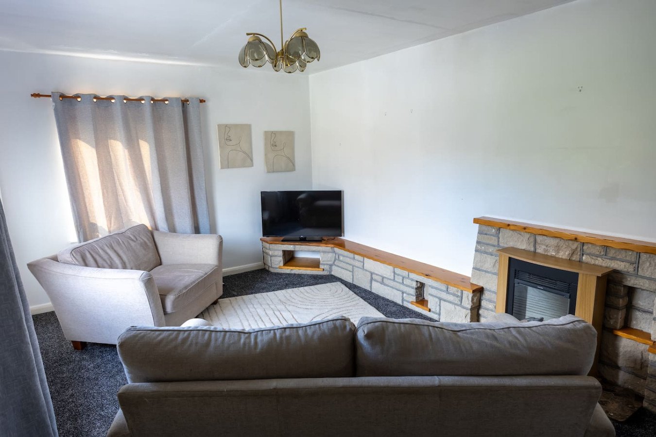 Living room with brown leather sofa, grey armchair, fireplace and wall-mounted TV