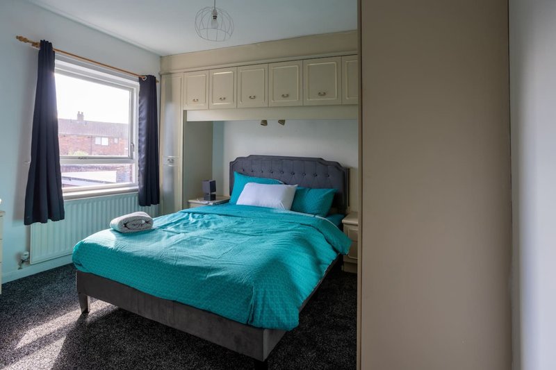 Bedroom with turquoise bedding, built-in wardrobes, window with dark curtains and radiator