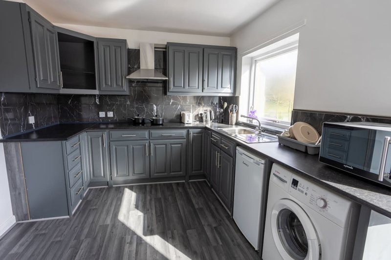 Modern kitchen with grey cabinetry, black countertops, white appliances and washing machine