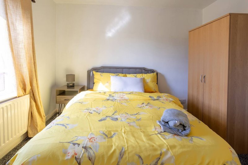 Bedroom with yellow floral duvet, wooden wardrobe, bedside table and window with golden curtains