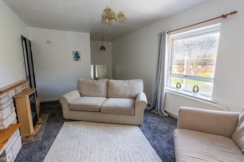 Light living room with beige sofa, armchair, fireplace and large window with garden view