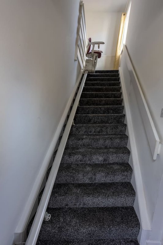 Narrow staircase with dark grey carpet, white walls, metal handrail and landing above