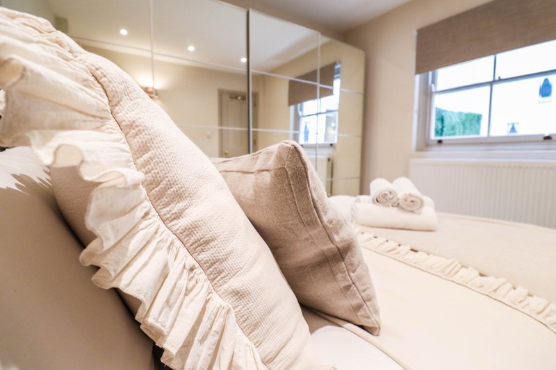 Modern bedroom with bed, cream pillows, white duvet and ensuite bathroom visible