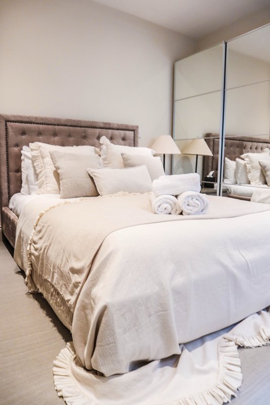 Neutral bedroom with double bed, upholstered headboard, mirrored wardrobe and bedside lamp