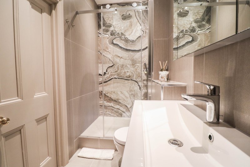 Modern bathroom with white vanity sink, toilet, and walk-in shower with marble tile