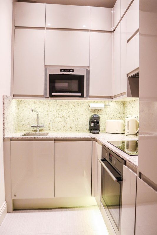 Modern compact kitchen with white cabinetry, stainless steel appliances, and granite countertop