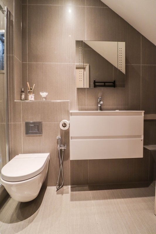 Modern bathroom with wall-mounted toilet, white vanity sink, tiled walls and heated towel rail