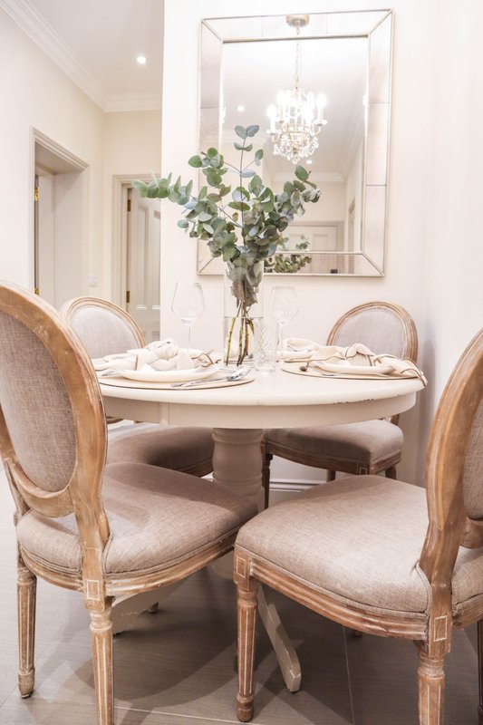 Elegant dining room with round white table, wooden chairs, fresh flowers, and large mirror above
