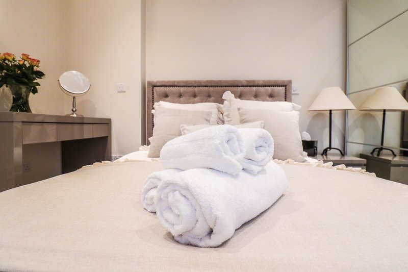 Bright bedroom with made bed, rolled white towels, bedside lamps and flowers