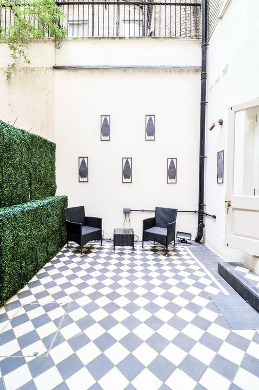 Courtyard patio with checkered flooring, black chairs, potted plants and wall sconces