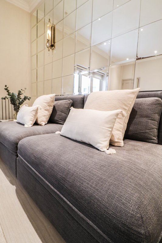 Modern bedroom with grey upholstered bed, cream and grey cushions, mirrored wall panels and pendant lighting