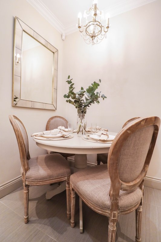 Elegant dining room with round table, two upholstered chairs, mirror, chandelier and floral arrangement