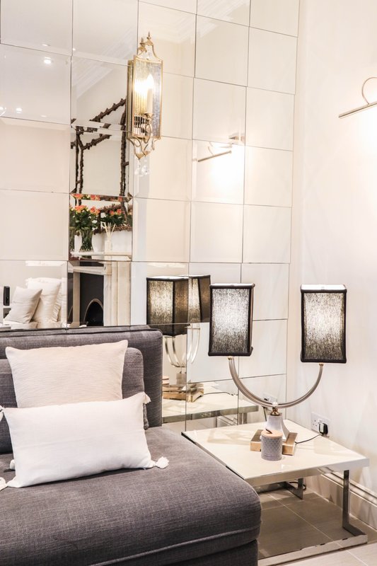 Modern bedroom with gray upholstered bed, white pillows, wall-mounted gold lighting fixtures, and decorative wall sconces