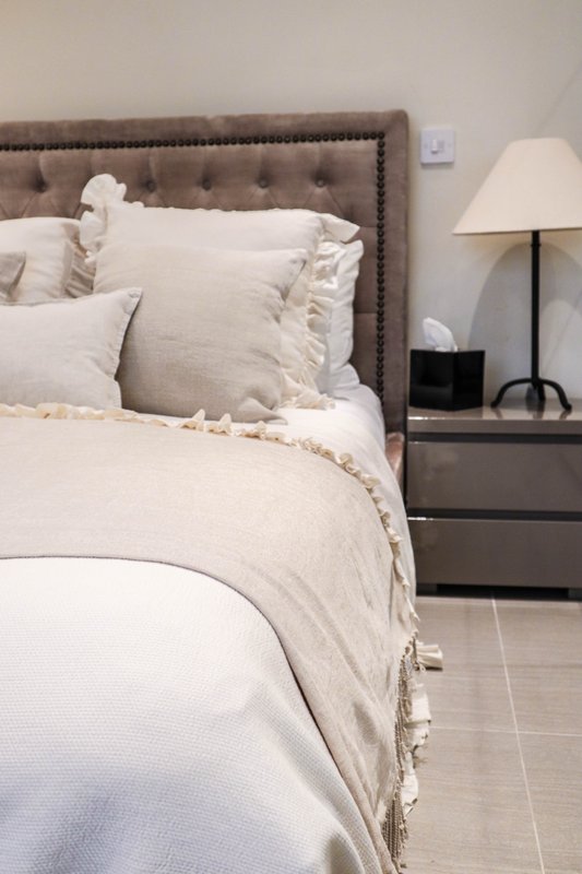 Bedroom with upholstered headboard, cream bedding, nightstand with lamp and decor