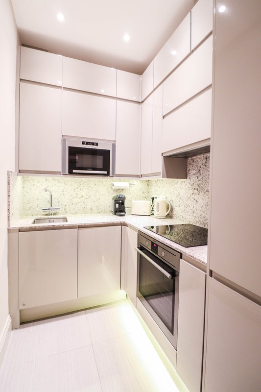 Modern white kitchen with built-in appliances, granite countertop, and LED lighting