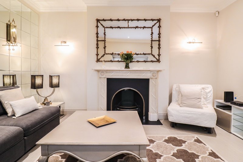 Modern living room with fireplace, gray sofa, white armchair, and decorative mirror above mantelpiece