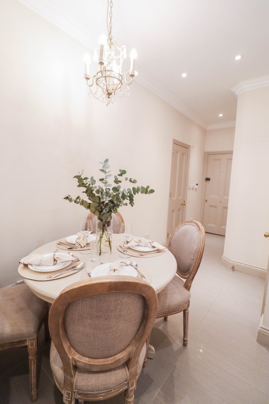 Elegant dining room with round white table, upholstered chairs, crystal chandelier and fresh flowers