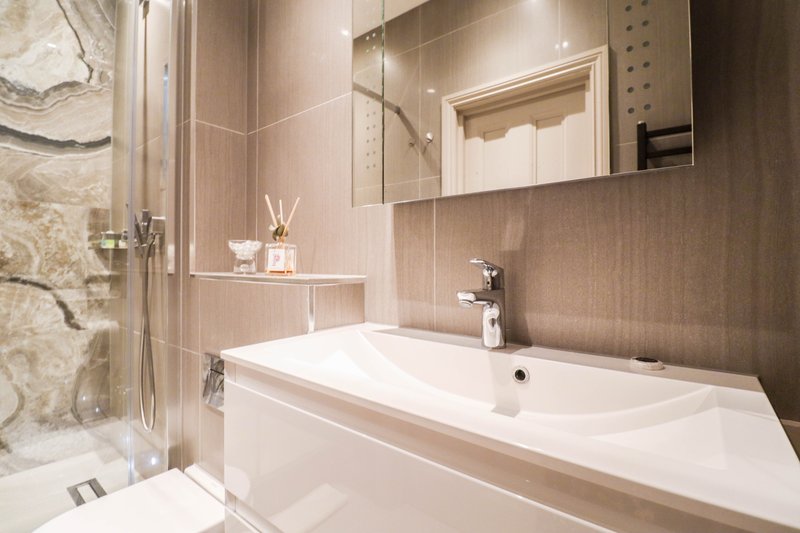 Modern bathroom with vanity sink, mirror, shower enclosure and beige tile walls