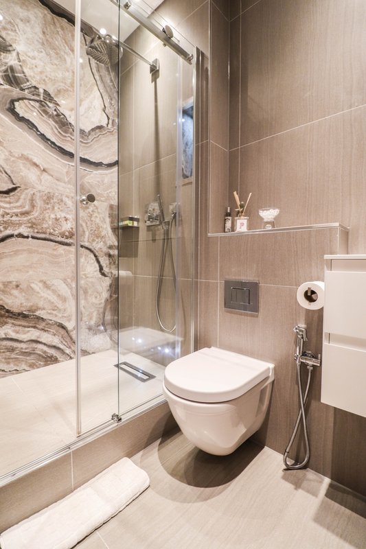 Modern bathroom with walk-in shower, wall-mounted toilet, and beige marble tile