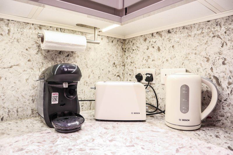 Kitchen countertop with black coffee machine, white toaster, white kettle and paper towel holder